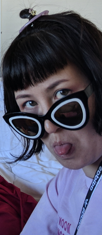 Pamela looking toward the camera over her sunglasses and sticking her tongue out